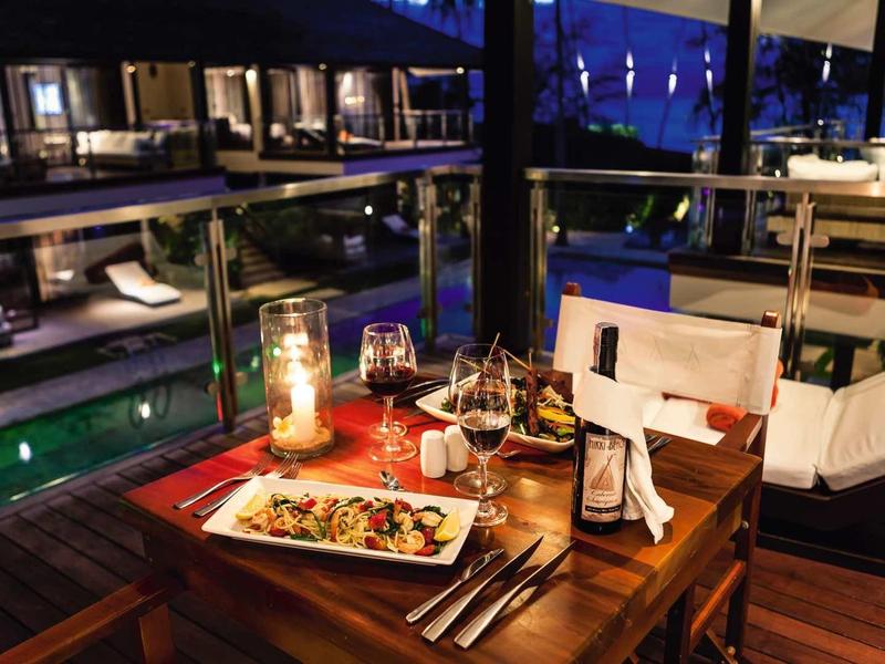 Elegante diner op een terras met uitzicht op een verlicht zwembad 's nachts.