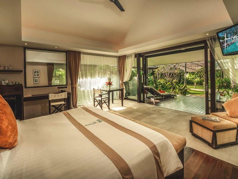 Lichte hotelsuite met groot bed, zithoek en open uitzicht op groene terras.