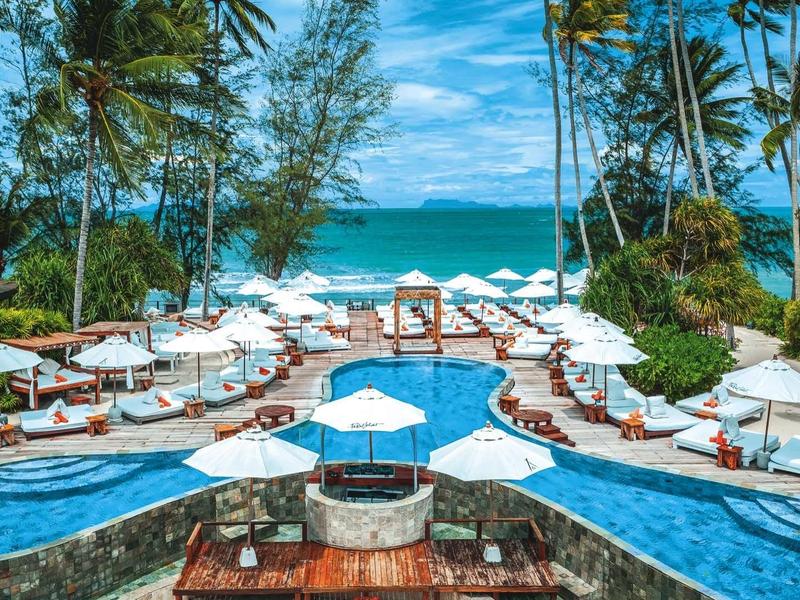 Luxe zwembadgedeelte met ligstoelen en parasols, omgeven door palmbomen aan zee.