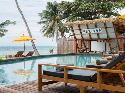 Moderne Liegestühle am Pool mit Blick auf das Meer und Palmen in einem Resort.