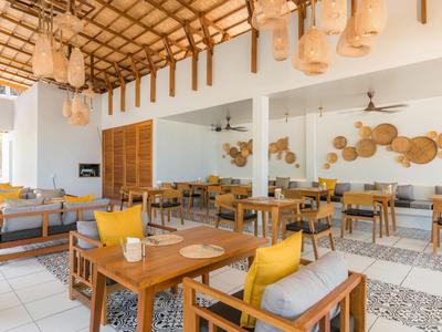 Helles Restaurant mit Holzmöbeln, gelben Kissen und dekorativen Körben an der Wand.