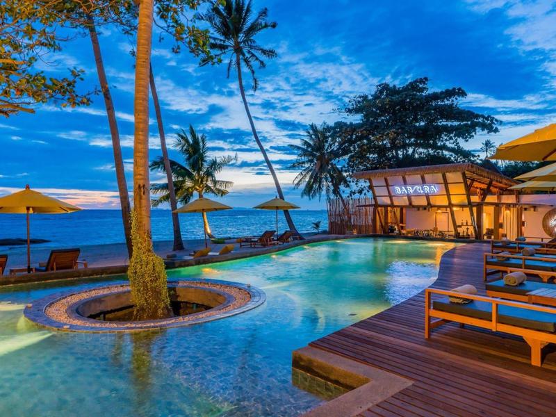 Poolbereich am Strand mit Palmen, Liegestühlen und Sonnenschirmen bei Sonnenuntergang.