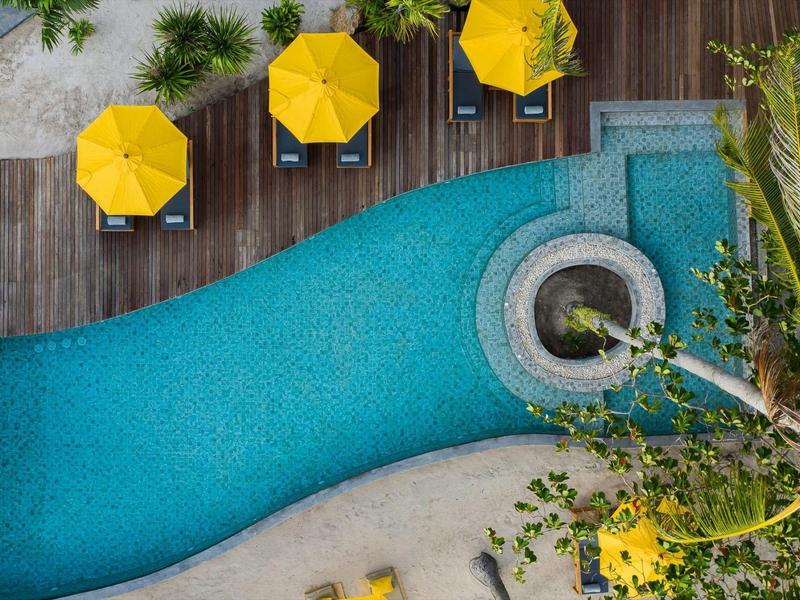 Blaue Poollandschaft mit runden Whirlpools, gelben Sonnenschirmen und Holzterrasse von oben.