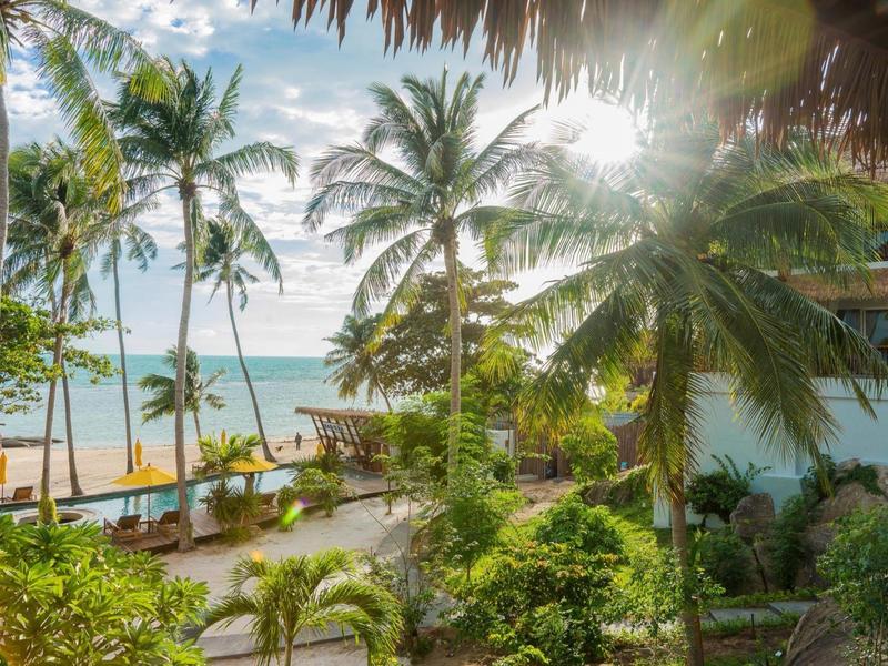 Tropischer Strand mit Palmen, grünem Garten und blauer See unter hellem Sonnenschein.
