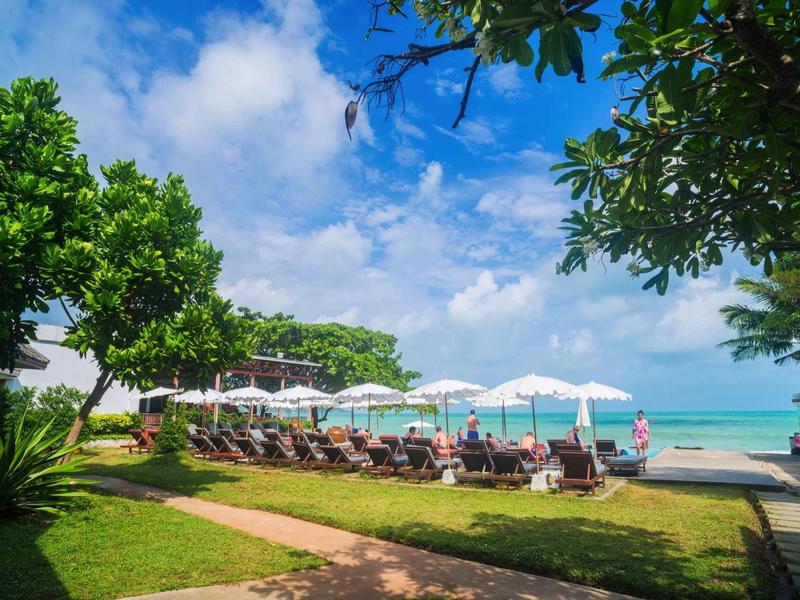 Ośrodek nad morzem z leżakami i parasolami obok tropikalnej zieleni i widokiem na ocean.