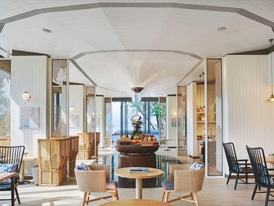 Helles, modernes Café mit Holz- und weißen Möbeln, großen Fenstern und Pflanzen im Hintergrund.