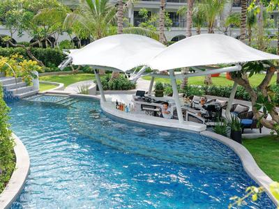 Venkovní bazén s barem pod dvěma velkými bílými plachtami v tropické zahradě.