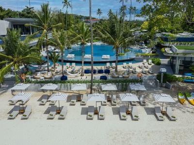 Bílá písečná pláž s lehátky, slunečníky, palmami a bazénem v tropickém hotelu.