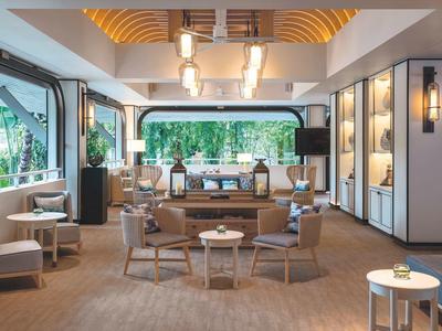 Světlý hotelový salonek s pohodlnými křesly, moderním dekorem a velkými okny.