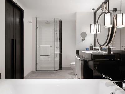 Moderní koupelna se skleněným sprchovým koutem, černým umyvadlem a bílou vanou.