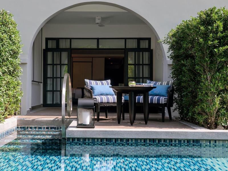 Elegantní venkovní posezení s bazénem před obloukovou terasou a zelenými keři.