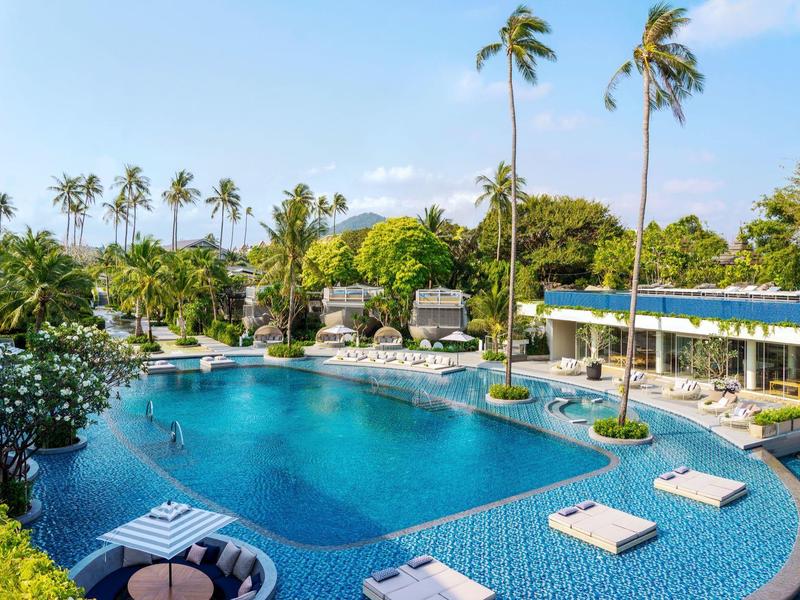 Azurový bazén obklopený palmami, s bílými lehátky a jasnou oblohou.