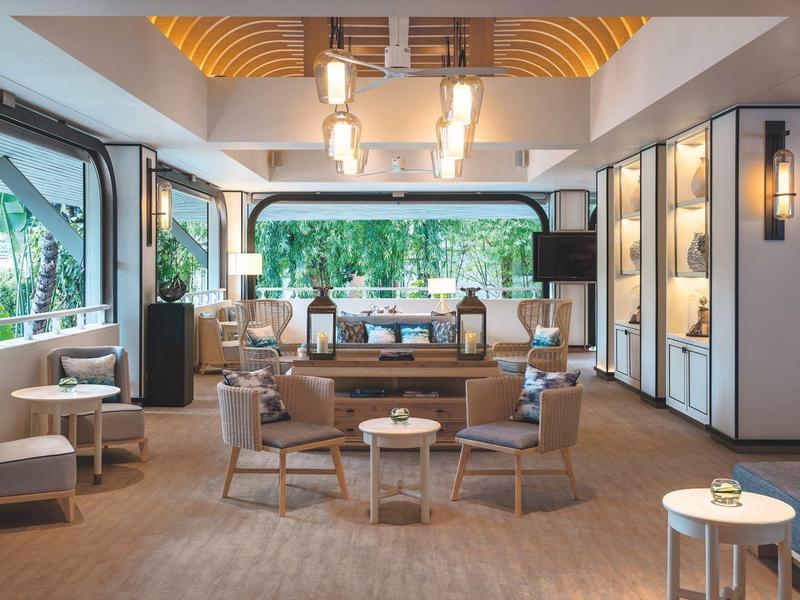Světlý hotelový salonek s pohodlnými křesly, moderním dekorem a velkými okny.