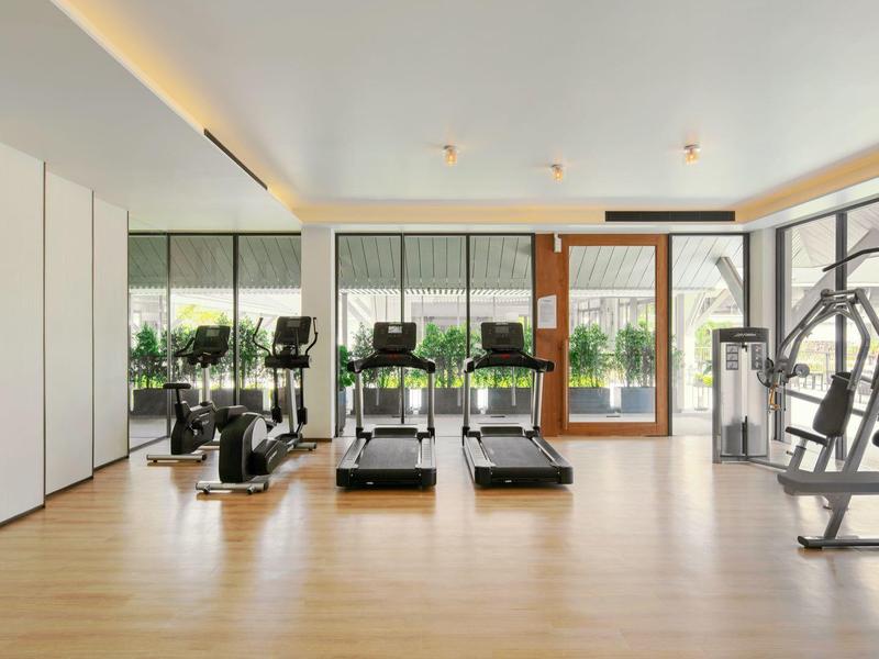 Moderní posilovna s fitness vybavením a velkými okny s výhledem do zahrady.