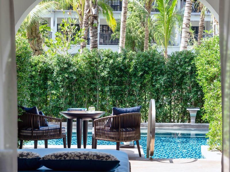 Terasa s stolem a křesly u bazénu, obklopena bujnou zelení.