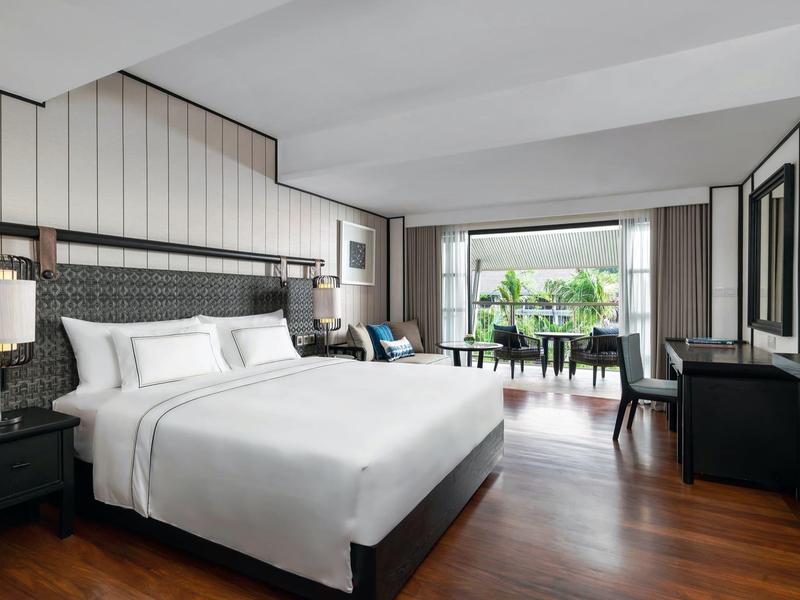 Elegantní hotelový pokoj s velkou postelí, dřevěnou podlahou a světlým balkonem s výhledem na zeleň.