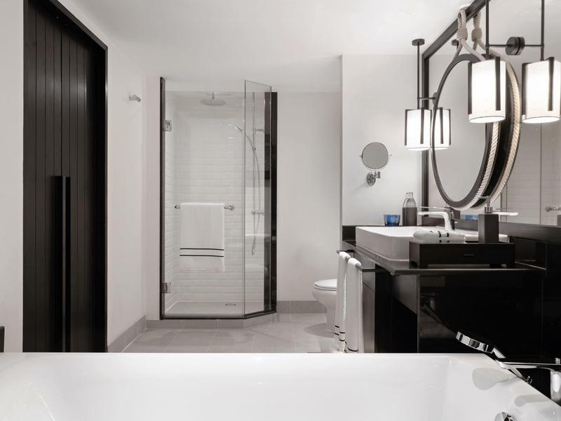 Moderní koupelna se skleněným sprchovým koutem, černým umyvadlem a bílou vanou.