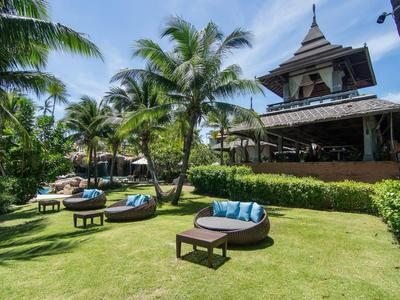Jardin luxuriant avec des palmiers, des sièges confortables et un pavillon spacieux sous un ciel bleu.