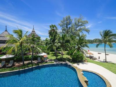 Une piscine d'hôtel tropicale avec des palmiers près d'une plage de sable blanc sous un ciel bleu clair.