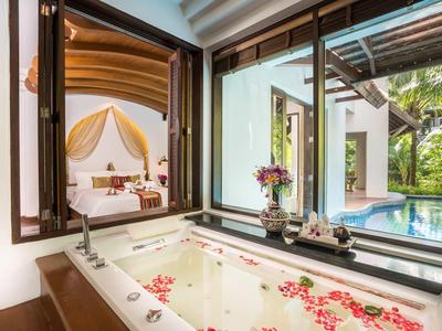 Baignoire luxueuse avec pétales de roses donnant sur piscine privée et chambre.