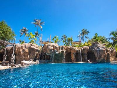 Großer Außenpool mit Felsen, Wasserfall und Palmen bei klarem blauem Himmel.