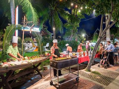 Marché nocturne avec stand de barbecue et vendeurs sous guirlandes lumineuses en milieu tropical