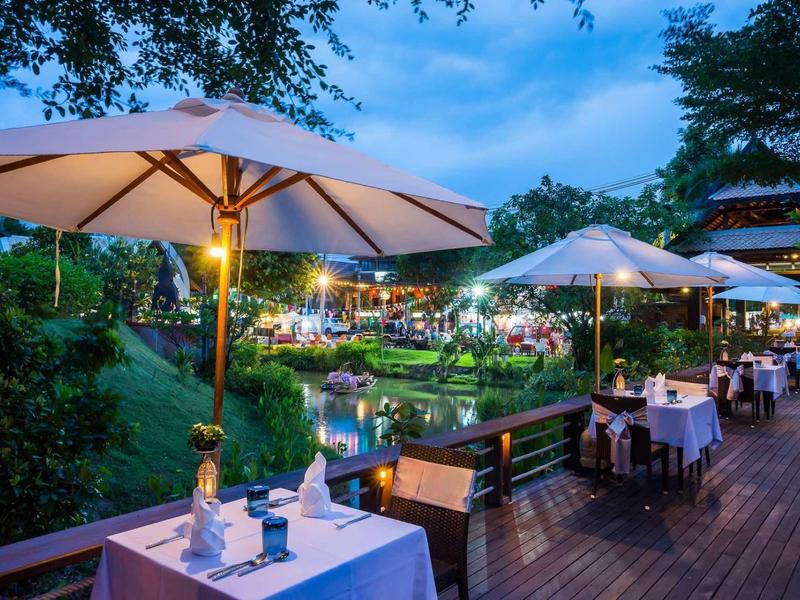 Terrasse de restaurant en soirée avec tables dressées et parasols dans un jardin verdoyant