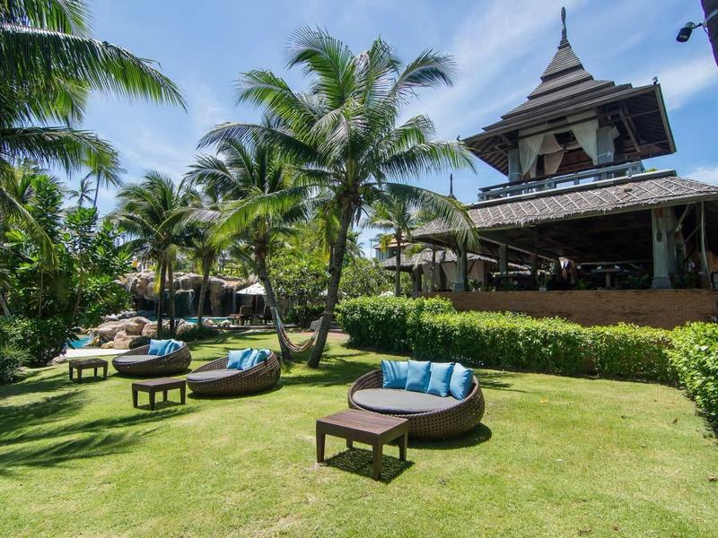 Jardin luxuriant avec des palmiers, des sièges confortables et un pavillon spacieux sous un ciel bleu.