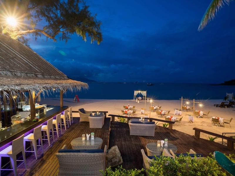 Bar côtière avec sièges, plage éclairée et océan la nuit.