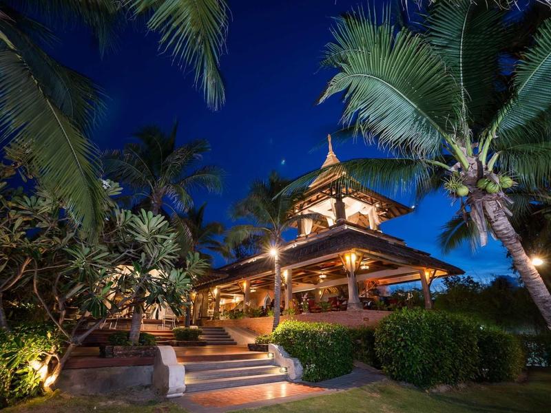 Complexe tropical éclairé la nuit avec des palmiers et des allées illuminées.