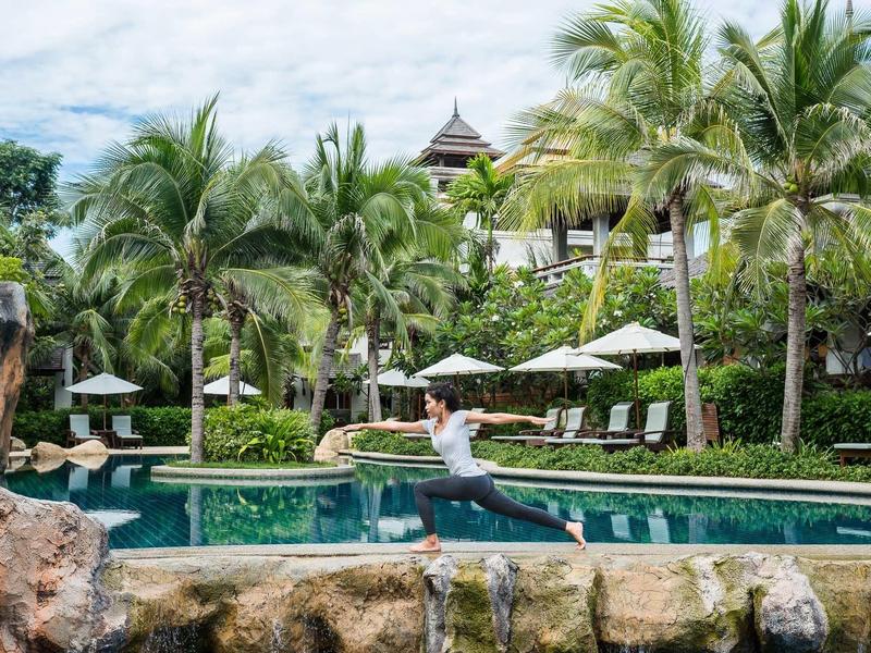 Personne sautant près de la piscine dans une station tropicale avec palmiers et chaises longues.