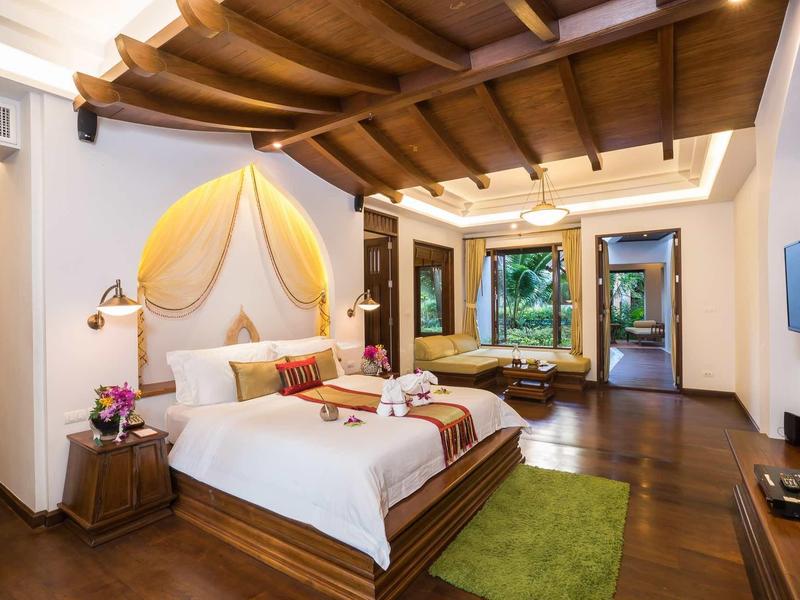 Chambre d'hôtel élégante avec sol en bois, lit double et coin salon près de la fenêtre.