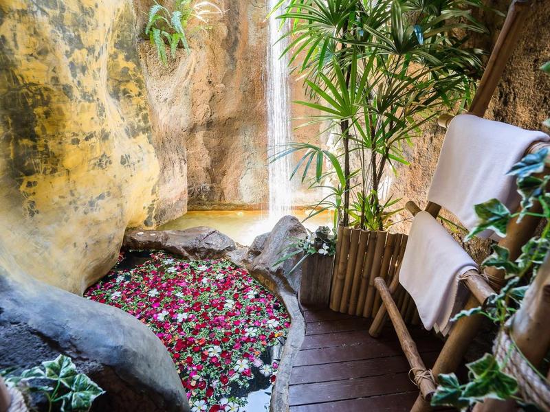 Espace spa chaleureux avec sol en bois, plantes et bassin d'eau rempli de pétales de rose.