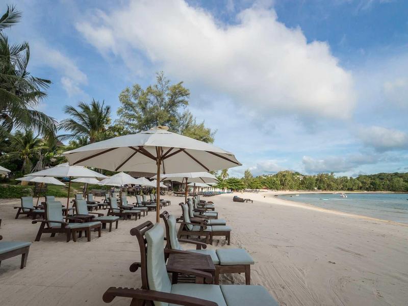 Plage avec chaises longues et parasols blancs à côté de la mer claire et ciel nuageux.