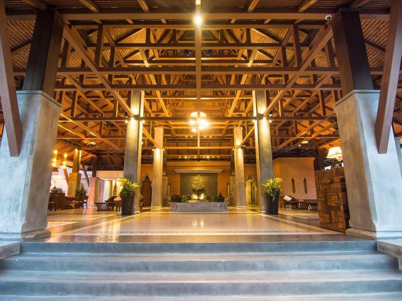 Grande réception d'hôtel ouverte avec poutres en bois apparentes et éclairage chaud.