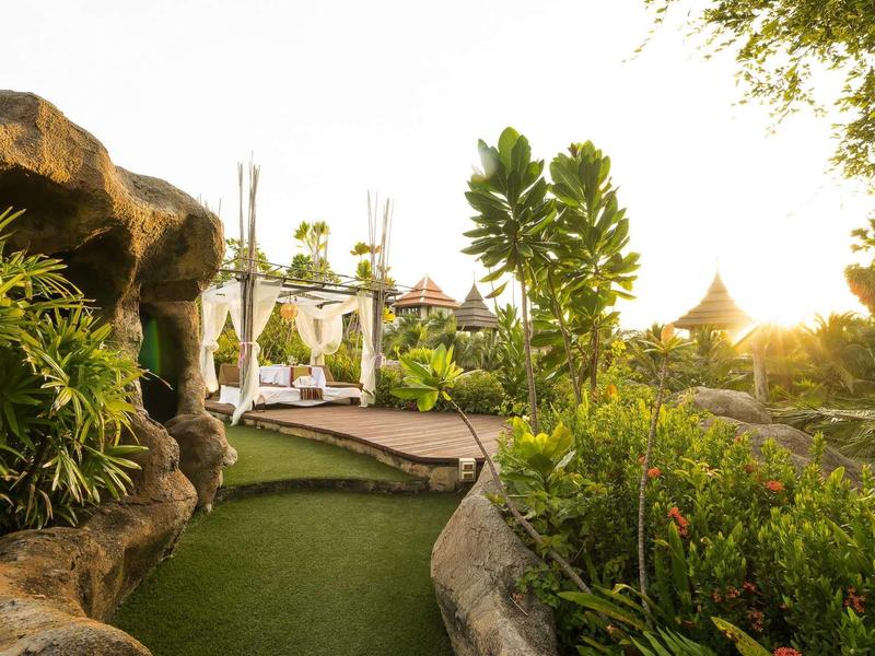 Jardin ensoleillé avec transats et plantes tropicales dans une station de vacances.