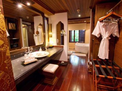 Luxusní hotelová koupelna s dřevěnou podlahou, velkým zrcadlem, vanou a věšákem na oblečení.