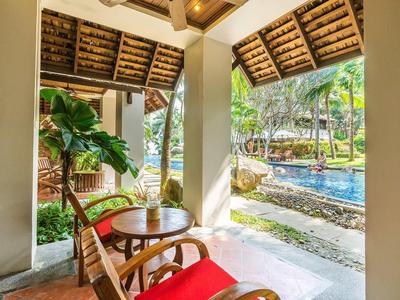 Pohodlný balkón s závěsným křeslem, dřevěným stolem, rostlinou a výhledem na bazén a zahradu.