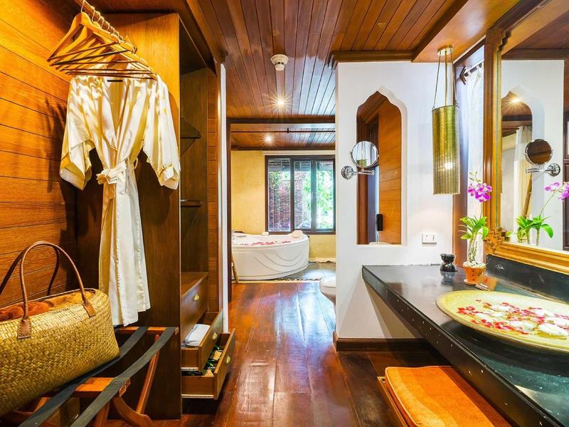 Moderní hotelový pokoj se dřevěným obkladem, otevřeným věšákem na oblečení a volně stojící vanou.