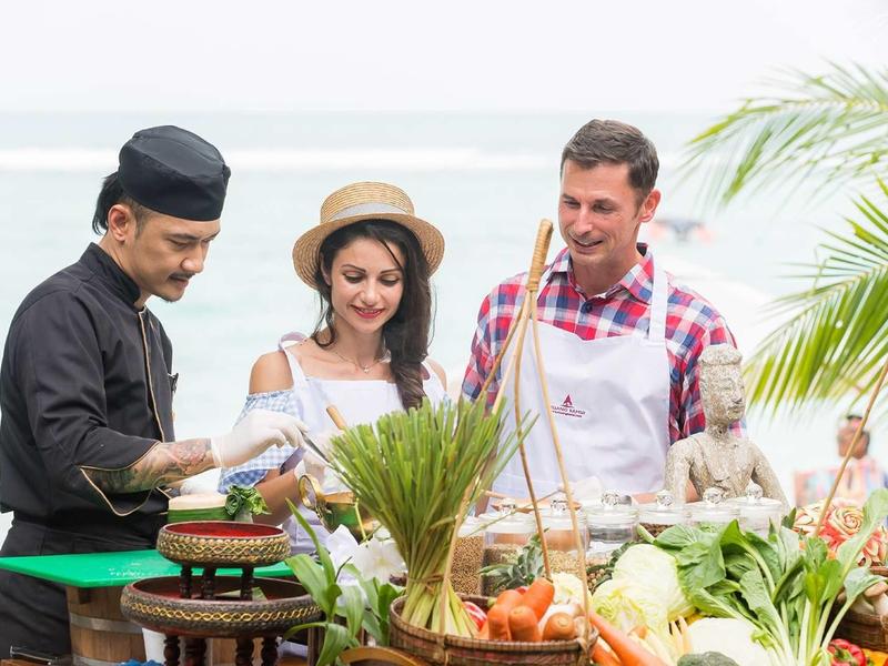 Tři lidé v lehkém dovolenkovém oblečení společně vaří venku u moře.