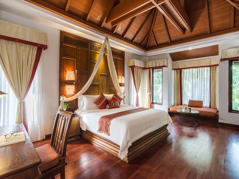 Elegantní hotelový pokoj s dřevěnou podlahou, manželskou postelí, psacím stolem a velkými závěsy.