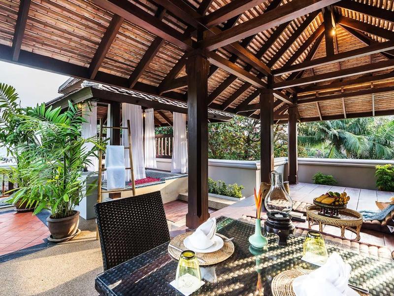 Zastřešená terasa s dřevěnou střechou, sezením a rostlinami v tropickém prostředí.