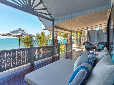 Überdachte Terrasse mit Sitzbereich, Blick auf Palmen und das Meer im Hintergrund.