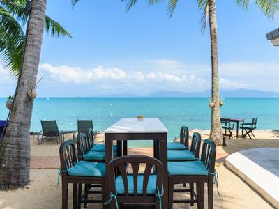 Stół jadalny z krzesłami na plaży pod palmami z widokiem na niebieskie morze.