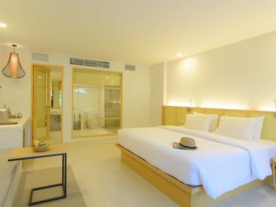 Nowoczesny pokój hotelowy z dużym łóżkiem podwójnym, jasnym wnętrzem i szklaną ścianą łazienki.