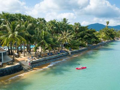 Strand mit Palmen, Steinmauer und ruhigem türkisfarbenem Wasser unter bewölktem Himmel