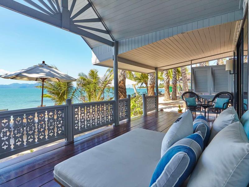 Zadaszony taras z meblami wypoczynkowymi, widokiem na morze i palmy pod czystym niebem.