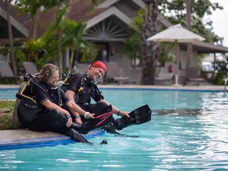 Dwóch nurków siedzi na krawędzi basenu z ekipmentem do nurkowania.