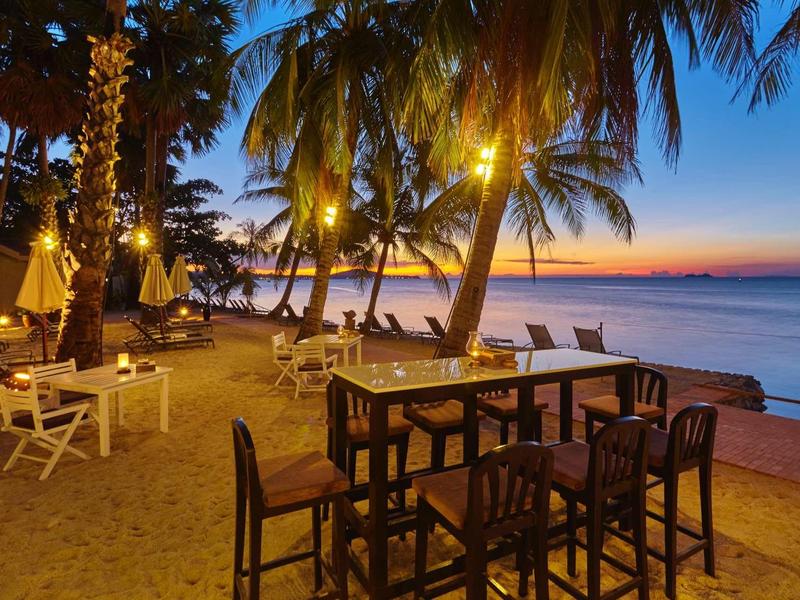 Plażowy bar z krzesłami i stołami pod palmami o zachodzie słońca przy morzu.