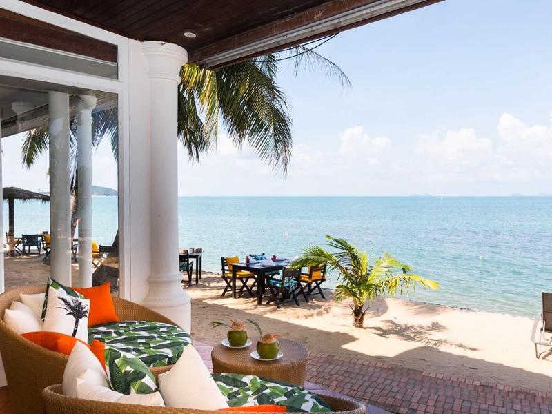 Widok z zadaszonego tarasu z miejscem do siedzenia na plażę i morze pod niebieskim niebem.